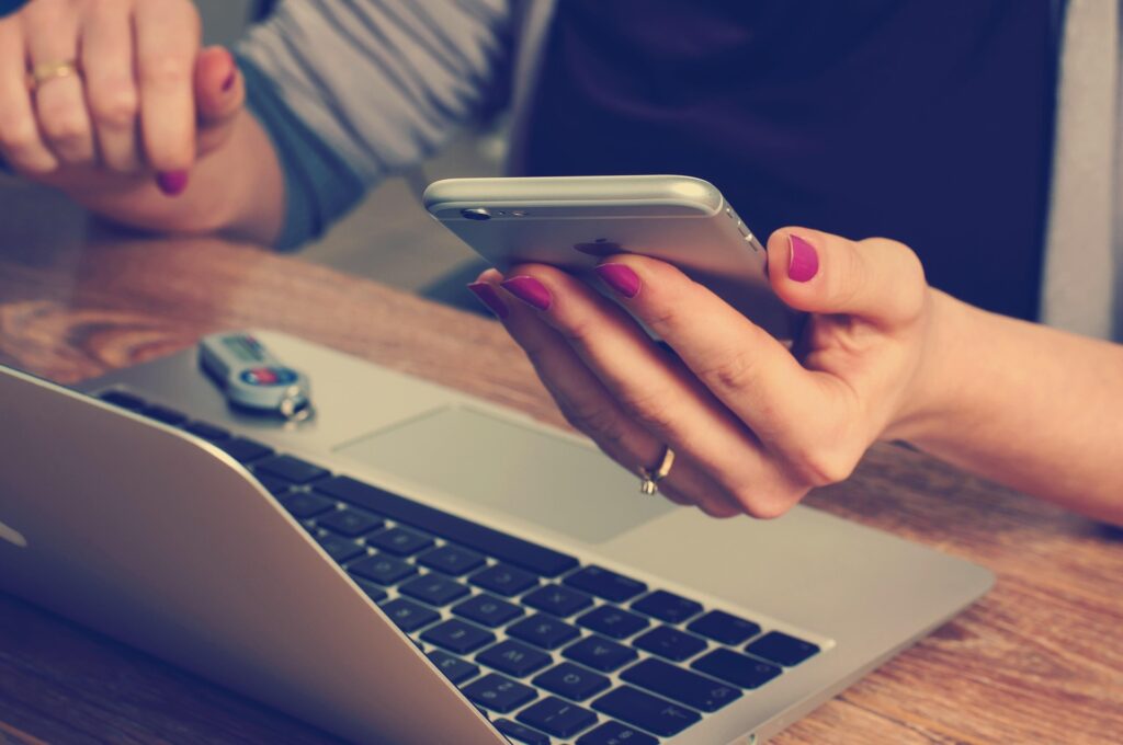 A female holding a phone with one hand sitting in front of her laptop